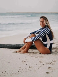 Woman sitting on beach in Long Sleeve swimsuit navy and white stripe sleeve | The Sulawesi in Nautical side view