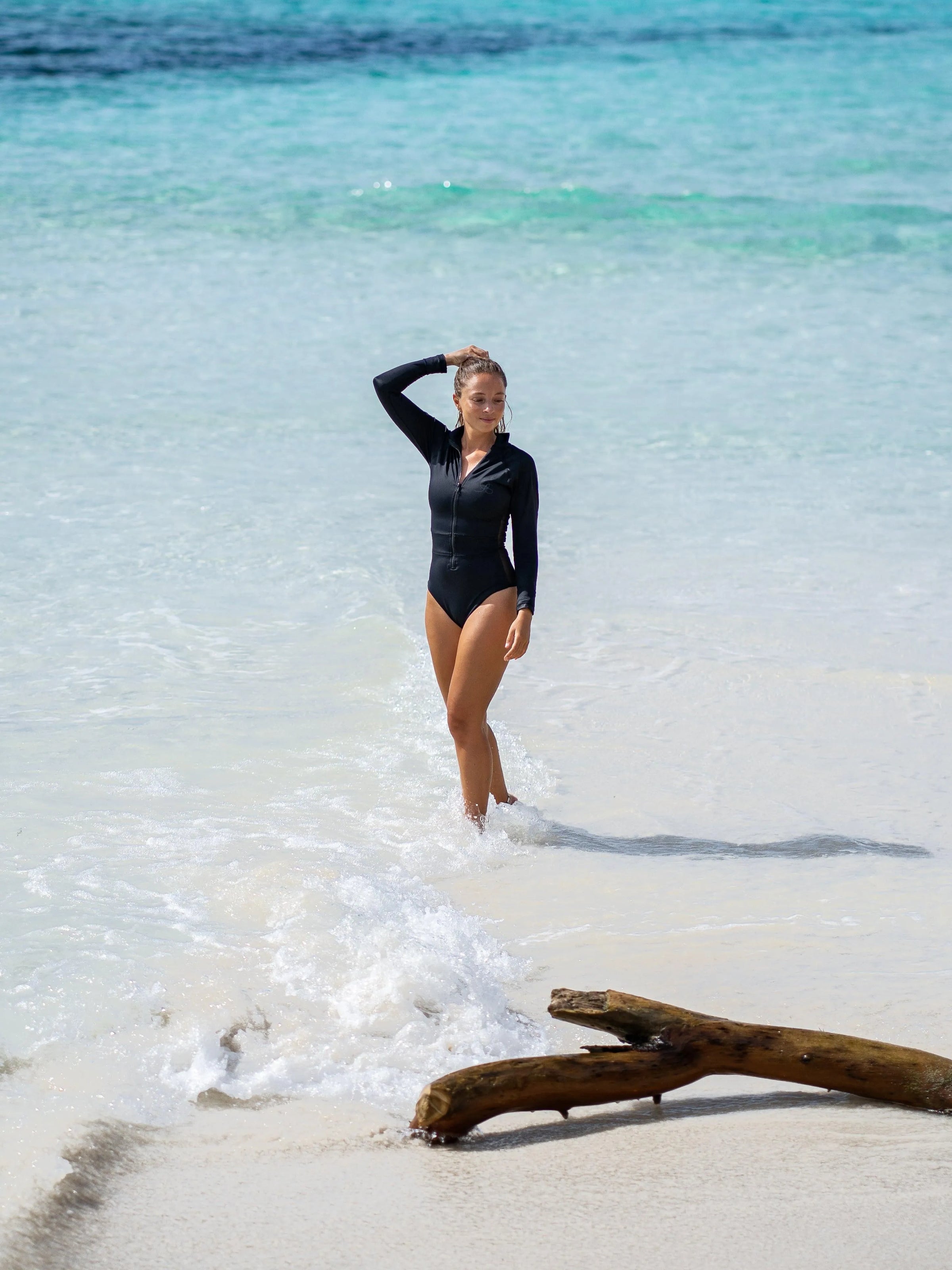 Woman standing in ocean wearing a Black Long Sleeve Surf Swimsuit | The Sulawesi Midnight-Ocean Soul Swimwear