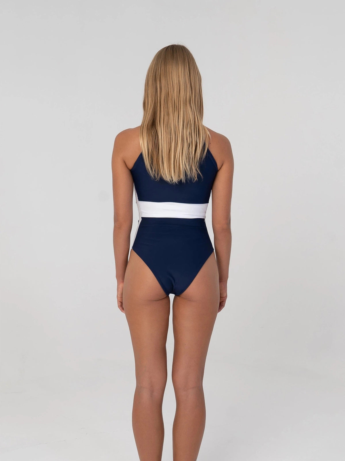 Navy blue one piece swimsuit with white accents on a white background, featuring text labels about fabric and design features.